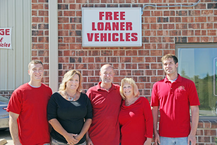 The 5th & Oak Autobody family under the Free Loaner Vehicles sign at the shop