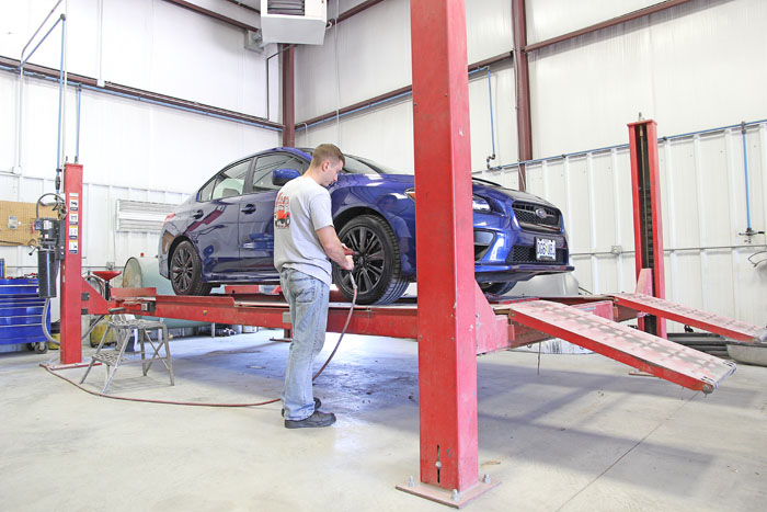 A 5th & Oak technician working on a car raised on a lift